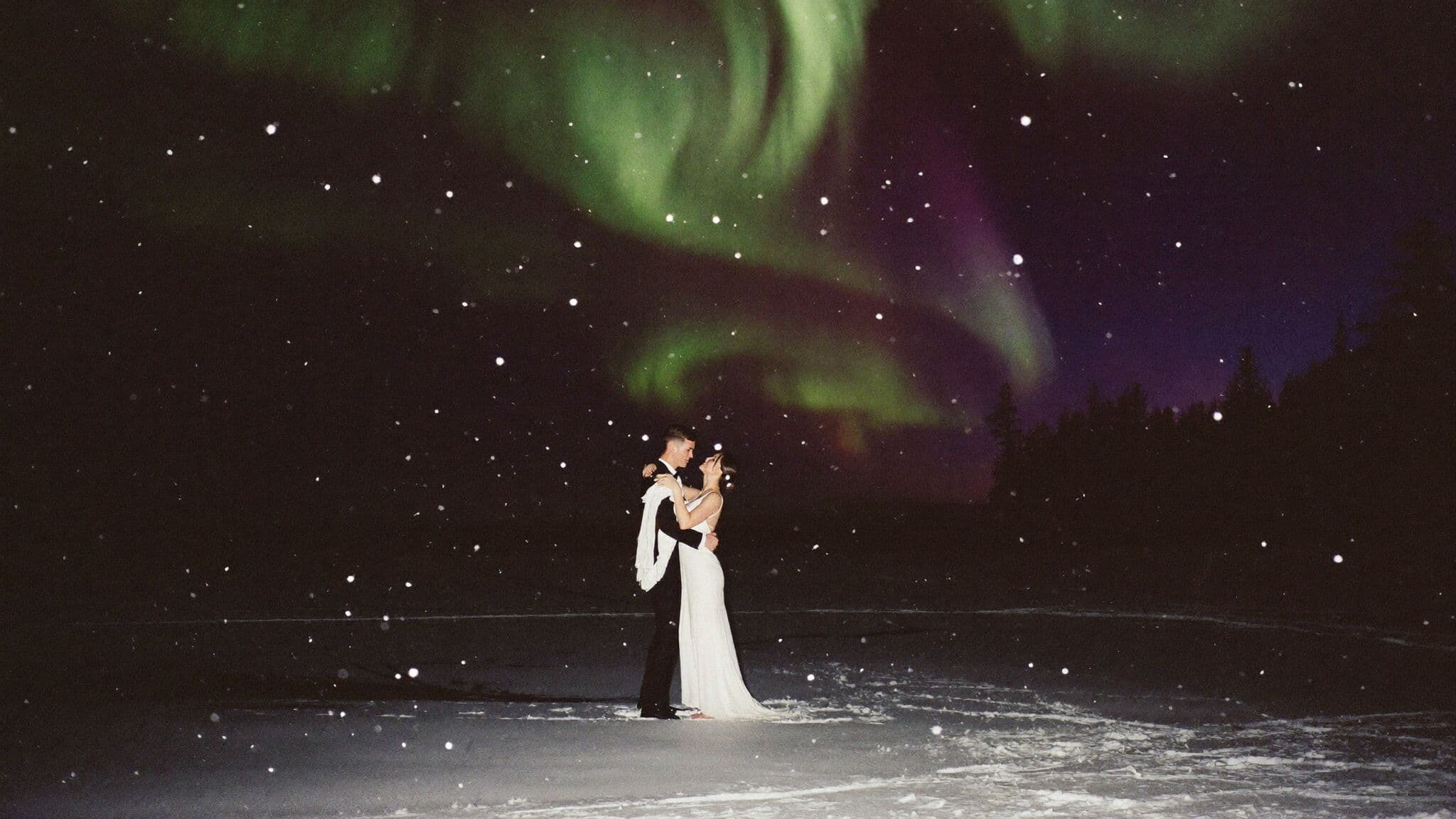Couple slow dancing on a frozen lake under the northern lights during a winter elopement