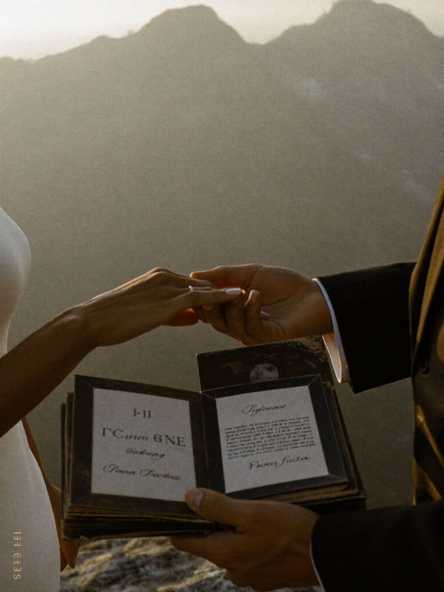 Couple exchanging rings with handwritten vow books on a windy mountain summit elopement