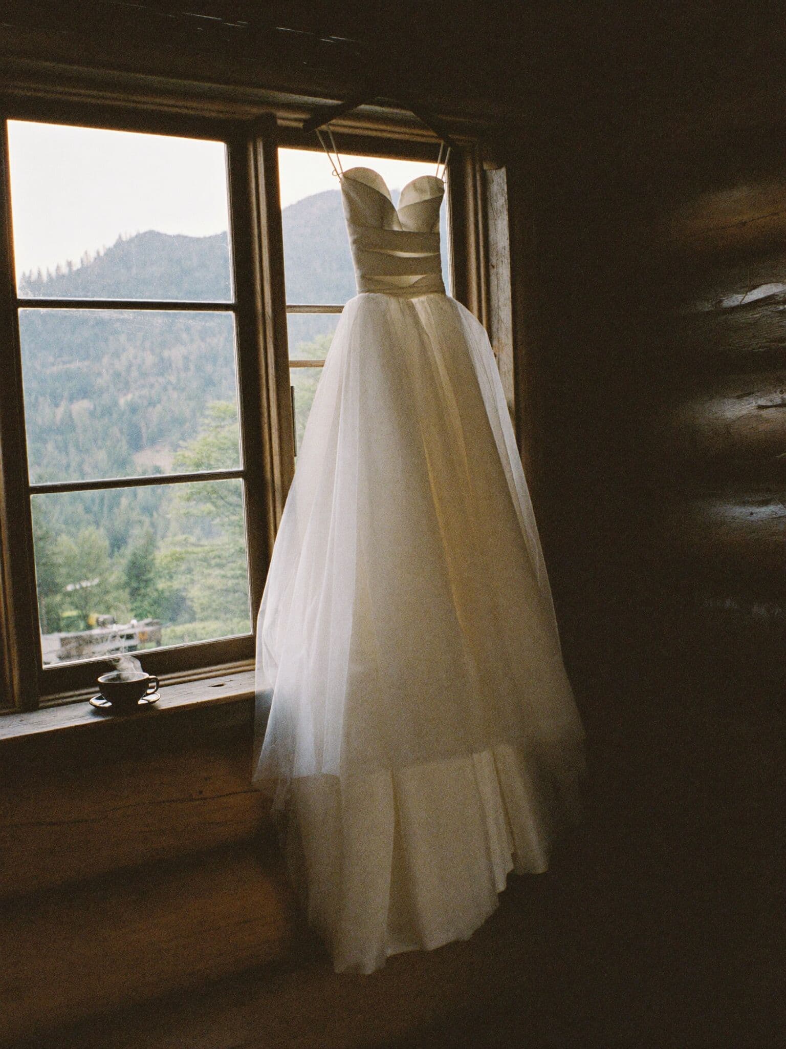Wedding dress hanging in the window of a timber cabin before an elopement