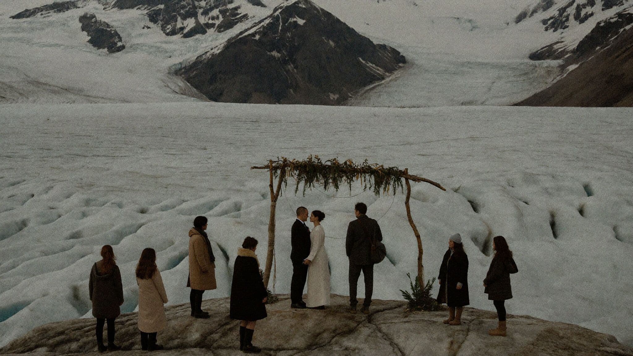 Intimate elopement ceremony for two on a glacier with mountains behind the couple