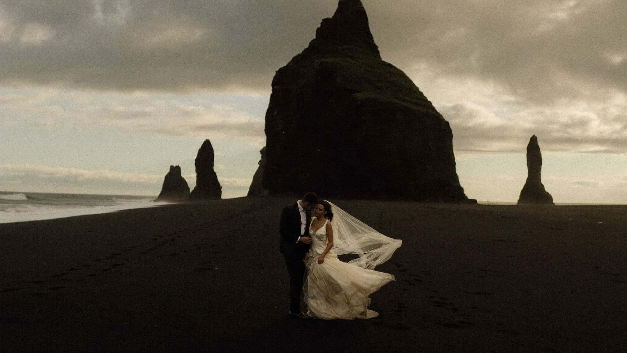 Bride and groom eloping on Reynisfjara black sand beach in Iceland, basalt sea stacks behind them