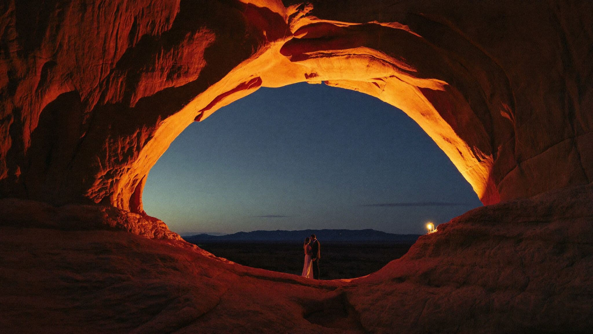 Eloping couple beneath Delicate Arch at sunrise in Arches National Park near Moab, Utah