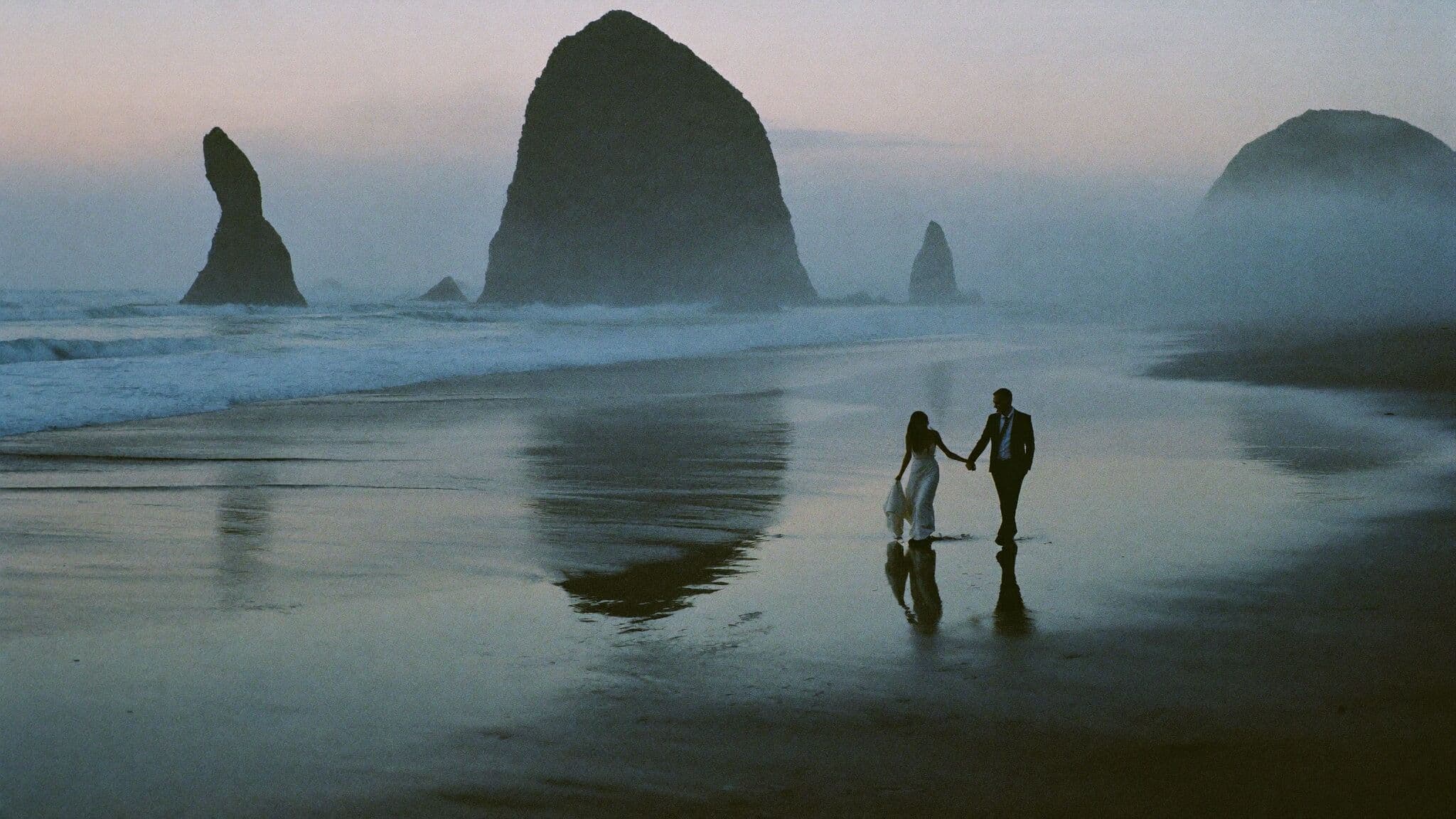 Couple walking past Haystack Rock at low tide during their Cannon Beach elopement in Oregon