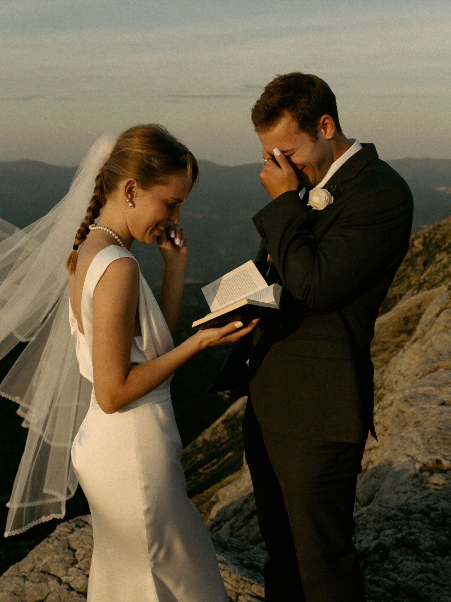 Bride reading vows from a leather book on a windy summit during an adventure elopement